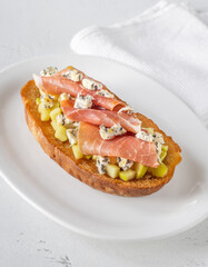 Toasted sandwich with blue cheese, prosciutto, sautéed apple, honey, white plate