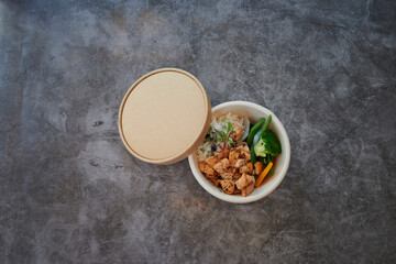 A bowl of food with a lid on top. The lid is brown. The bowl is white. The food is chicken and vegetables