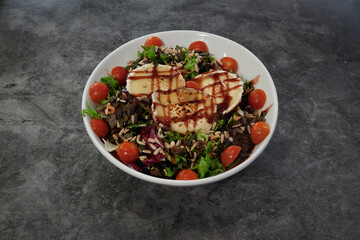 A white bowl with a salad in it. The salad has tomatoes, spinach, and cheese. There are three pieces of cheese in the salad