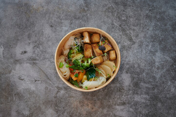 A bowl of food with vegetables and meat. The bowl is made of cardboard