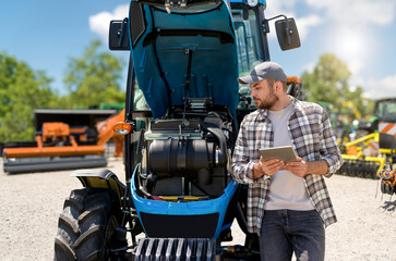 Male farmer using digital tablet to inspect tractor engine with modern technology. Agricultural...