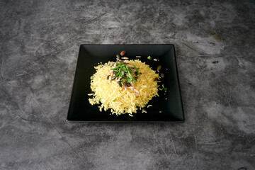 A plate of rice with nuts and herbs on top. The plate is black and the rice is yellow