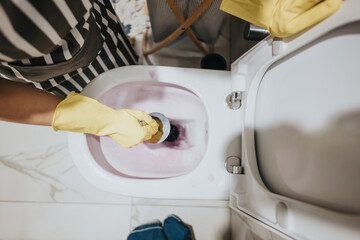 A close-up view of a toilet cleaning process with a gloved hand using a cleaning tool, showcasing...