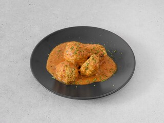 A plate of meatballs with a sauce on top. The sauce is red and has parsley in it