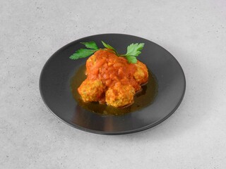 A plate of meatballs with a red sauce and parsley on top. The meatballs are arranged in a circular pattern, with some of them slightly overlapping each other