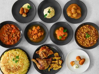 A table with many plates of food, including a plate of chicken and potatoes. There are also some bowls of food on the table