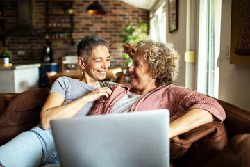 Senior lesbian couple using laptop on cozy couch at home