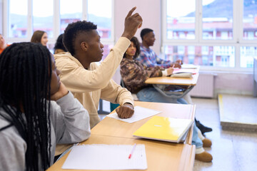 Young male student raising hand in classroom during lesson