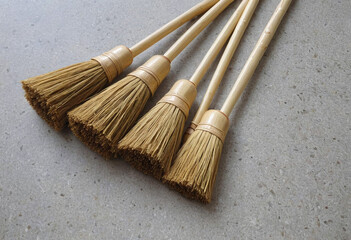Fototapeta premium Multiple straw brooms with wooden handles neatly arranged on a textured stone floor. Each broom showcases craftsmanship with natural materials for effective cleaning tasks