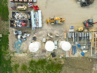 Drone top down view of a housing construction site. A single yellow tele hoist vehicle is parked ip near three tall white mortar silos at the lower part of the image. © Nick Beer