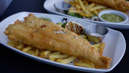 Crispy fried fish and chips with lemon and sauces resting on white plate