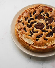 Homemade plum pie on a plate. Pie on a white stone textured background.