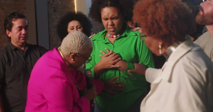 Female preacher blessing African American woman's belly during a spiritual gathering, group offering prayers and support for expecting mother in a compassionate church setting