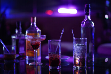 A close-up shot of various alcoholic beverages and bottles on a bar table under vibrant purple lighting, showcasing a nightlife ambiance.