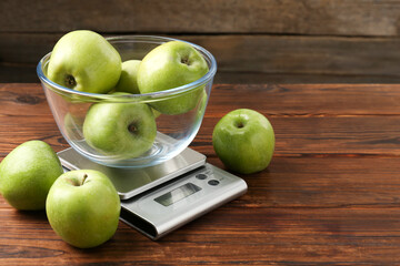Electronic kitchen scale with bowl of green apples on wooden table, closeup. Space for text