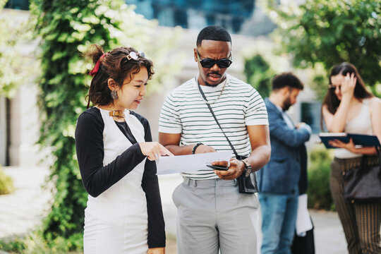A group of diverse professionals engaged in a casual outdoor business meeting, exchanging ideas and reviewing documents. The setting is relaxed, yet focused, indicative of modern business dynamics.