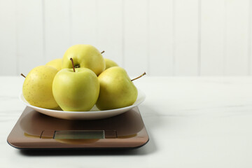 Modern electronic kitchen scale with apples on white marble table. Space for text
