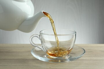 Pouring freshly brewed tea from teapot into cup at wooden table, closeup