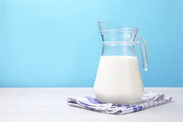 Fresh milk in jug on white wooden table against light blue background. Space for text