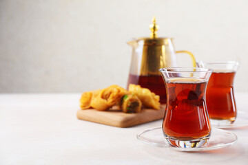 Traditional Turkish tea in glass cups, teapot and fresh baklava on white table, closeup. Space for text