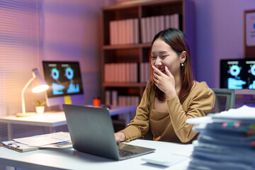 Young happy businesswoman laughing while using laptop, working late at night in office with computer and paperwork