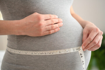 Close-up of pregnant belly being measured with a tape by woman hands. Symbol of love, care and body...