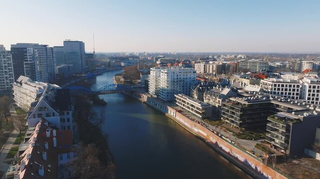Aerial view of Wroclaw, Poland, featuring the Oder River, a blue bridge, historic red roofed buildings, modern architecture, and green spaces.