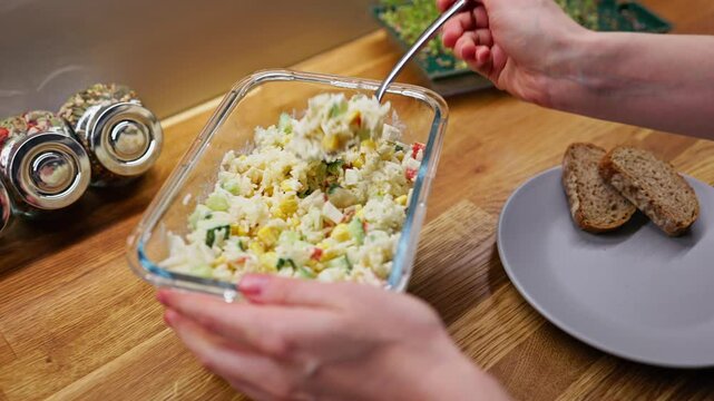 Culinary professional preparing gourmet crab salad with fresh corn, cucumber, and mayonnaise, served alongside crisp rye bread slices on rustic wooden surface. Chef crafting delicate crab salad 
