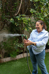 Happy senior woman watering garden with hose