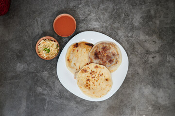 Three tortillas are on a white plate. A bowl of food is next to the plate. The bowl is filled with a red sauce