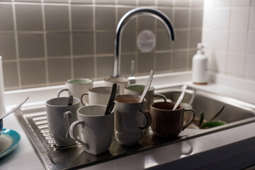 A kitchen sink with a lot of dirty dishes, mugs and plates.