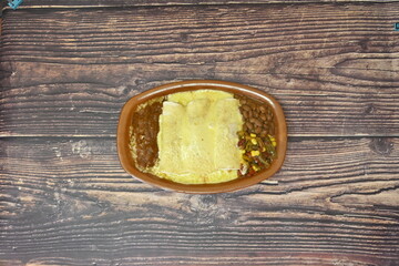 A bowl of food with beans and corn on a wooden table. The food is yellow and white