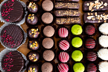 Assorted chocolate truffles and desserts with nuts and toppings on wooden surface