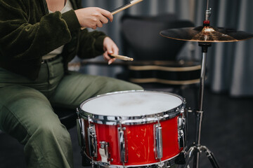 A close-up of a person playing a red drum set with focused precision during a music practice session in a professional studio environment.
