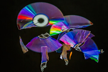 A broken compact disc shattered into many pieces with rainbow reflections on it, on a black background, close-up shot, data loss, old technology, loss of archival information.