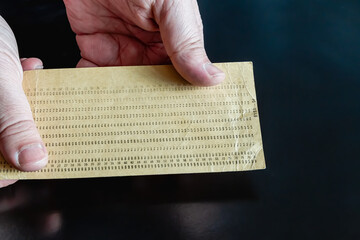 An old punch card in hands on a dark background, close-up shot, old technology, 20th-century...