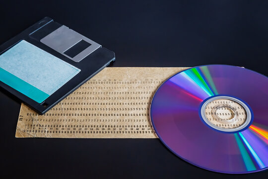 An old punch card, computer floppy disk, and compact disc on a dark background, showcasing outdated technology, 20th-century technology, early computer data, and an old archive.