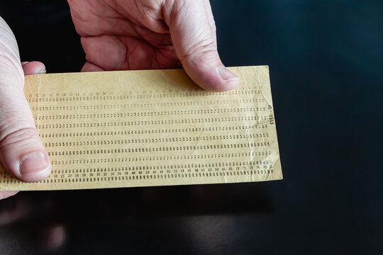 An old punch card in hands on a dark background, close-up shot, old technology, 20th-century technology, early computer data.