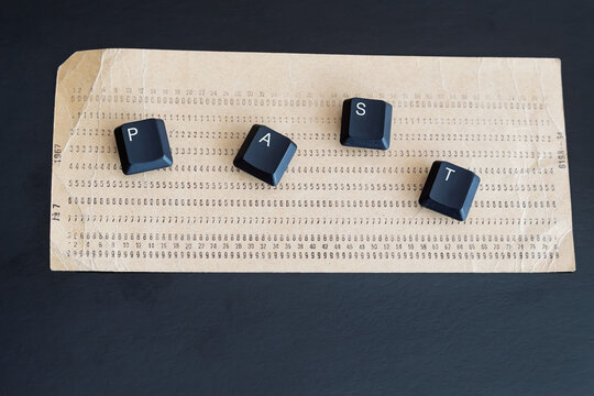 An old punch card with the word "past" made from computer keyboard keys on it, on a dark background, close-up shot, outdated technology