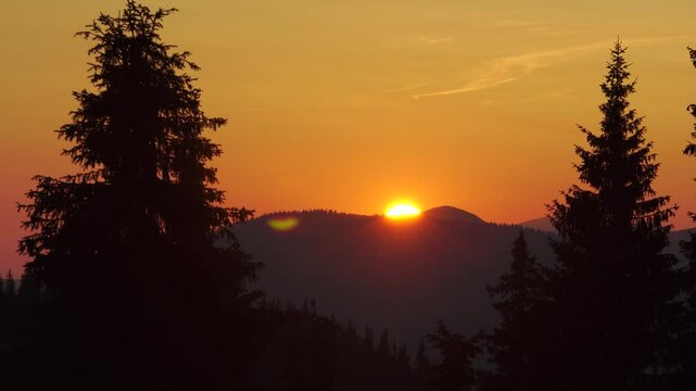 Orange sunset in mountains with pines in foreground timelapse