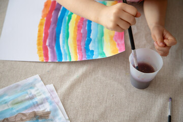 A child paints with watercolors, developing fine motor skills, creativity, and autonomy through...
