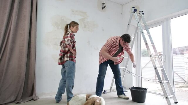 Happy couple renovating new house apartment , spackling wall. Cute dog calmly sleeping in the foreground on the floor. Home makeover, renovation concept. Family man woman repair house themselves.
