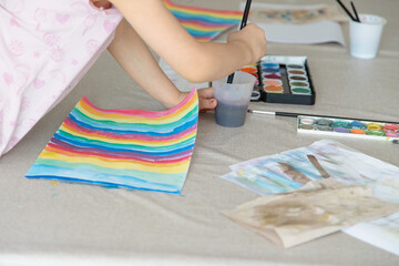 A child paints with watercolors, developing fine motor skills, creativity, and autonomy through...