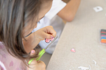 During a creative activity at home, a young child carefully uses safety scissors to cut out a heart...