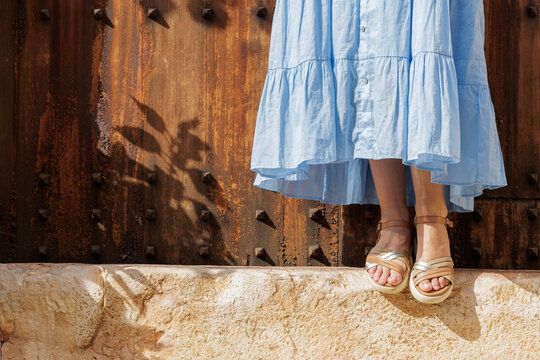 Close-up of a young woman's feet in sandals, resting on the step of a village gate on her vacation trip.