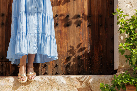 Close-up of a young woman's feet in sandals, resting on the step of a village gate on her vacation trip.