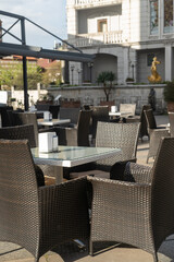 outdoor dining, wicker chairs and glass-topped tables adorn the outdoor seating area, set in front of an ornate building with a golden statue and potted plants, complete with a pergola