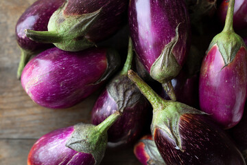 Dark purple eggplants with green stems lay scattered on a rustic wooden surface, showcasing their glossy skin and healthy appearance