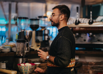 A man with glasses holding a beverage at a modern coffee shop bar, surrounded by brewing equipment and colorful decor, creating a cozy and inviting atmosphere.