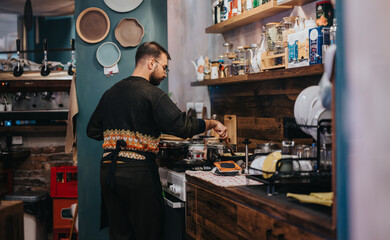 A chef focuses on cooking in a charming kitchen with wooden shelves featuring utensils and dishes. The workspace highlights a mix of tradition and modernity, capturing a scene of culinary artistry.